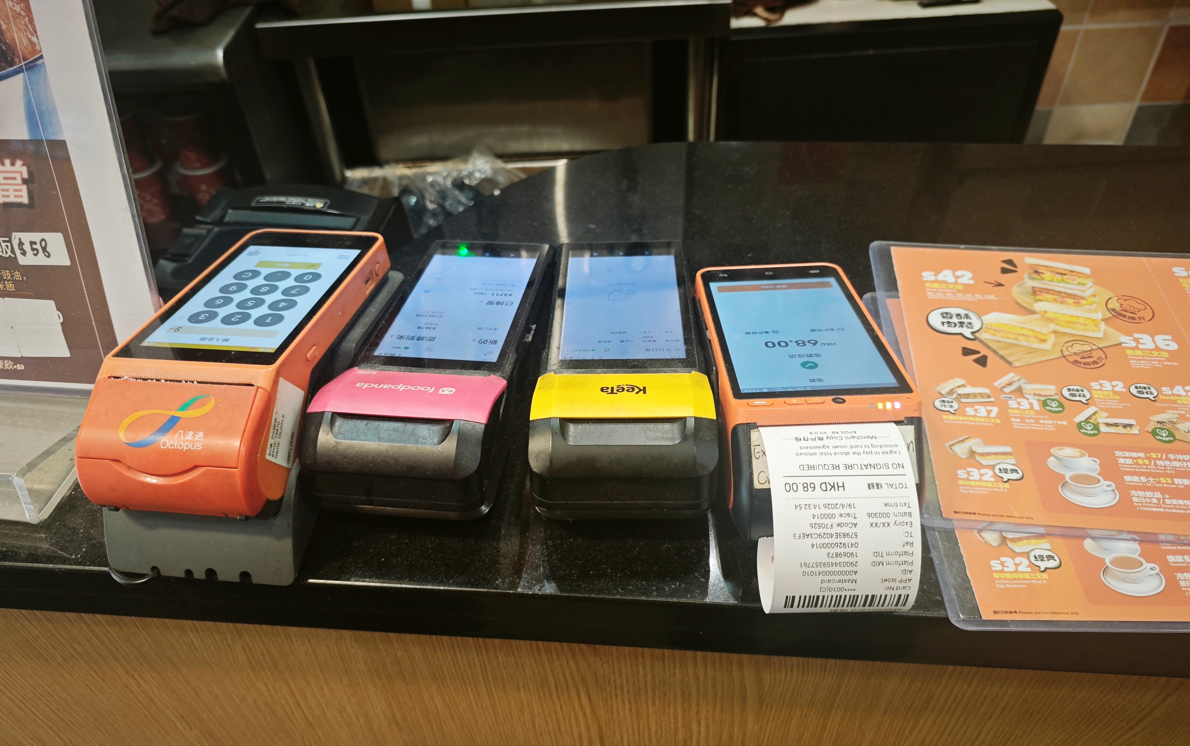 Order terminals from multiple delivery platforms line the counter at Guzzle Central, a sandwich shop in Central, April 19, 2026. Photo: Rita Liu